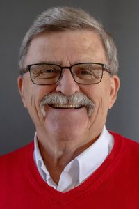 A photo of Gene Youngman in a red sweater, smiling at the camera