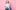 Ali Stroker, who is a wheelchair user, is posed in front of a pink background and wearing a white tshirt and blue jeans. She is smiling.